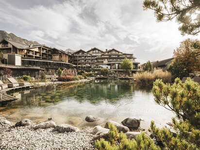 Wellnesshotel Der Engel mit Badesee im Vordergrund und Hotel im Hintergrund im Herbst