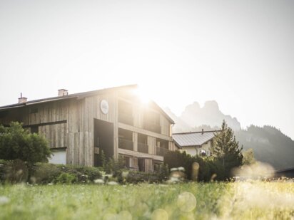 Suites am Kraut Garten - im Vordergrund die Wiese im Hintergrund das Suitenhaus darüber die aufgehende Sonne