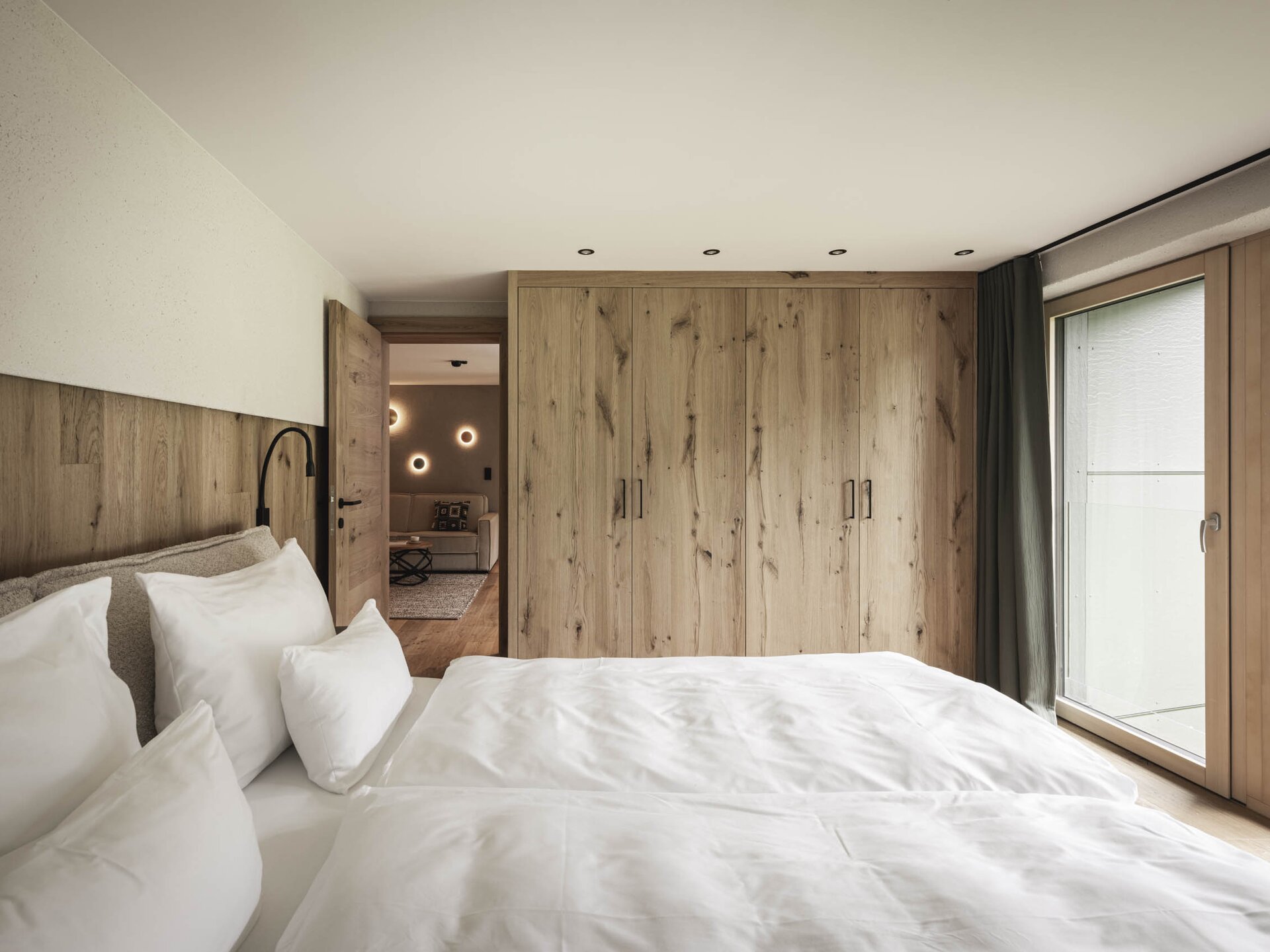 Masterbedroom mit Doppelbett und Kleiderschrank vor großem Panoramafenster mit Aussicht auf die Wiese vor dem Krautgarten
