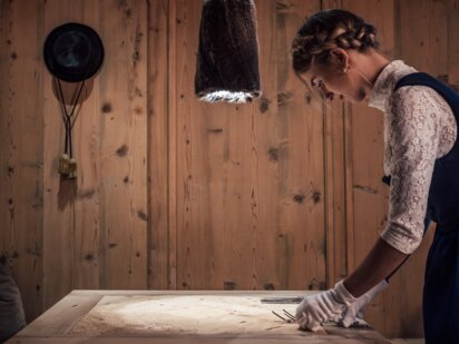 Person im traditionellen Tiroler Dirndl beim Eindecken eines Tisches in einer Tiroler Holzstube | Der Engel in Tirol