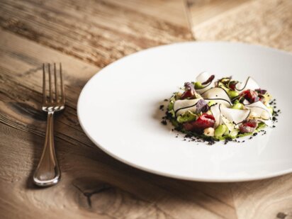 Reduzierter weißer Teller mit aufwendigem Fine Dining Gericht steht auf einem traditionellen Holztisch