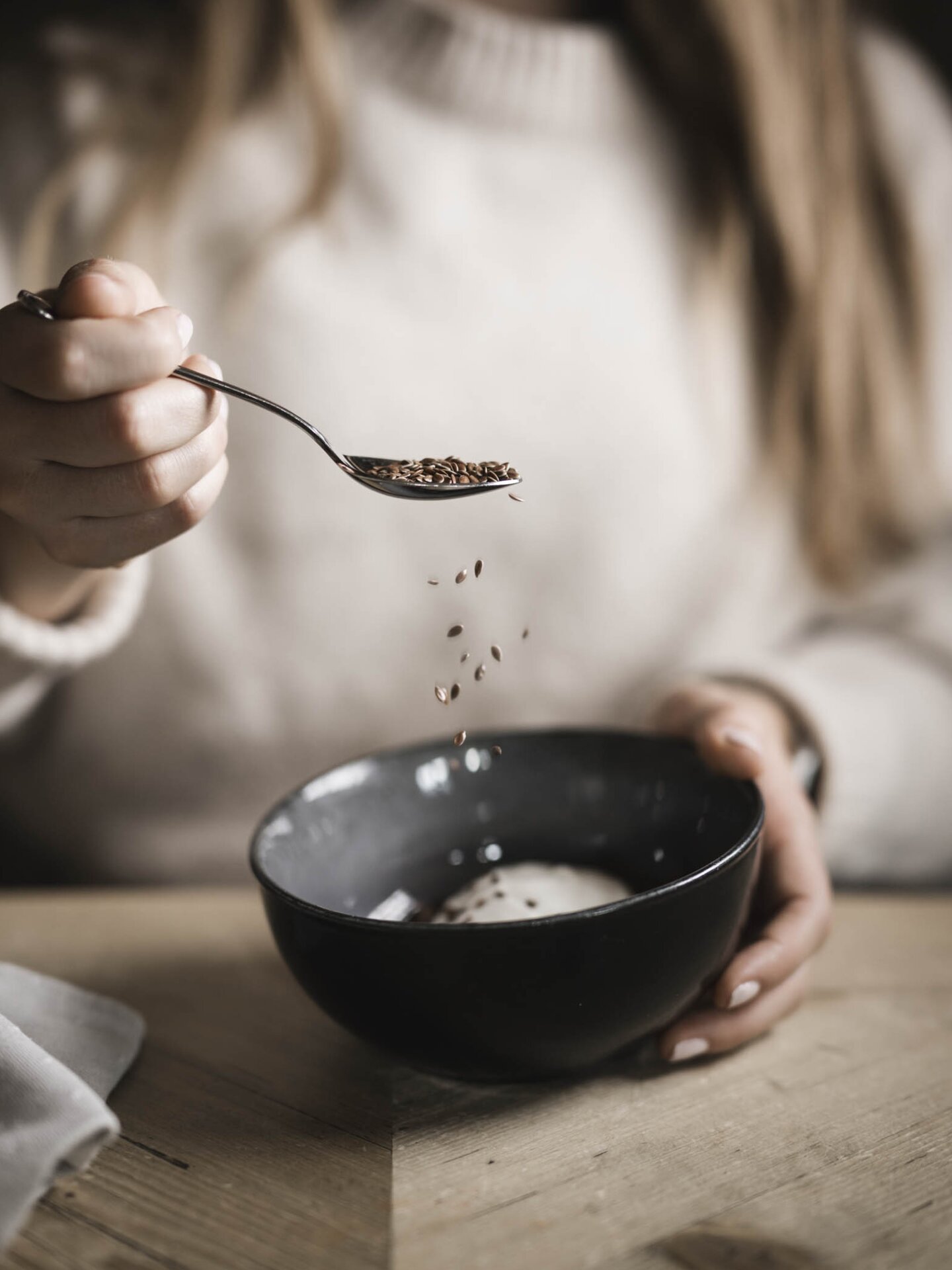 Gast hält Müslischüssel in der Hand und lässt Leinsamen in das Müsli fallen