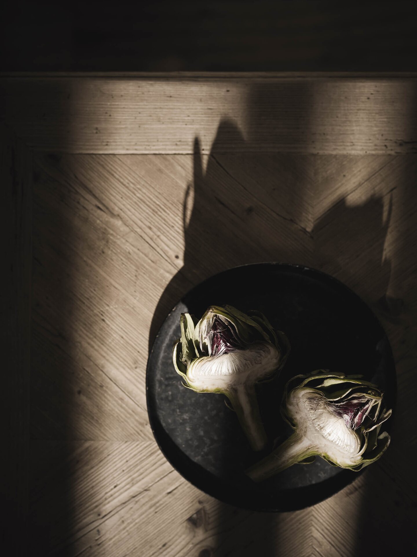 Halbierte Artischocke im Licht-Schatten-Spiel auf schwarzem Ton-Teller