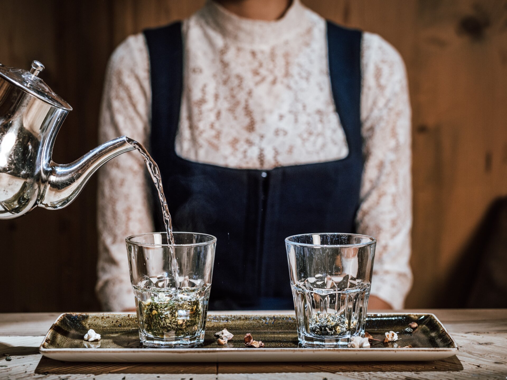 Tee eingießen in Glas im Hintergrund Person mit traditionellem Tiroler Dirndl | Der Engel in Tirol