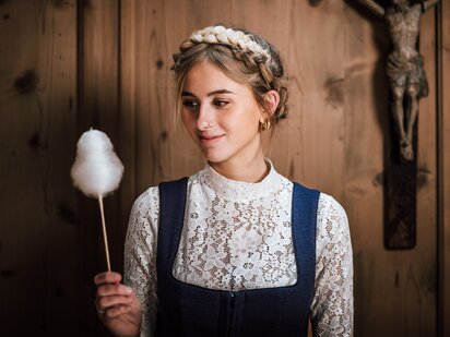 Person mit Zuckerwattestäbchen in traditionellem Tiroler Dirndl in einer Tiroler Stube | Der Engel in Tirol