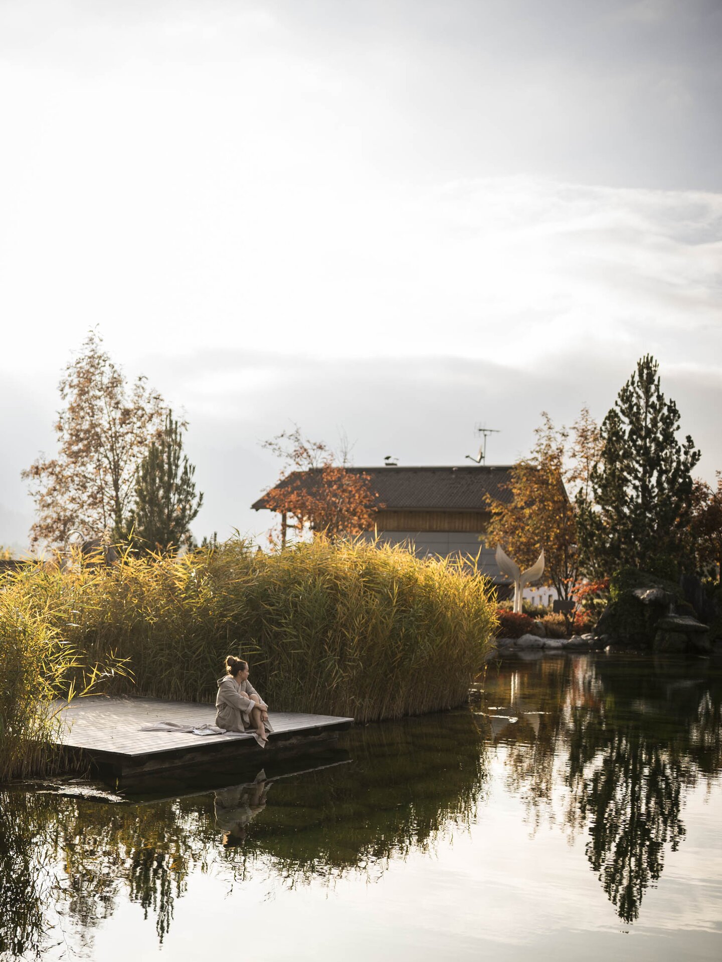 Person im Bademantel sitzt auf dem Steg des Engel Badesees im Herbst