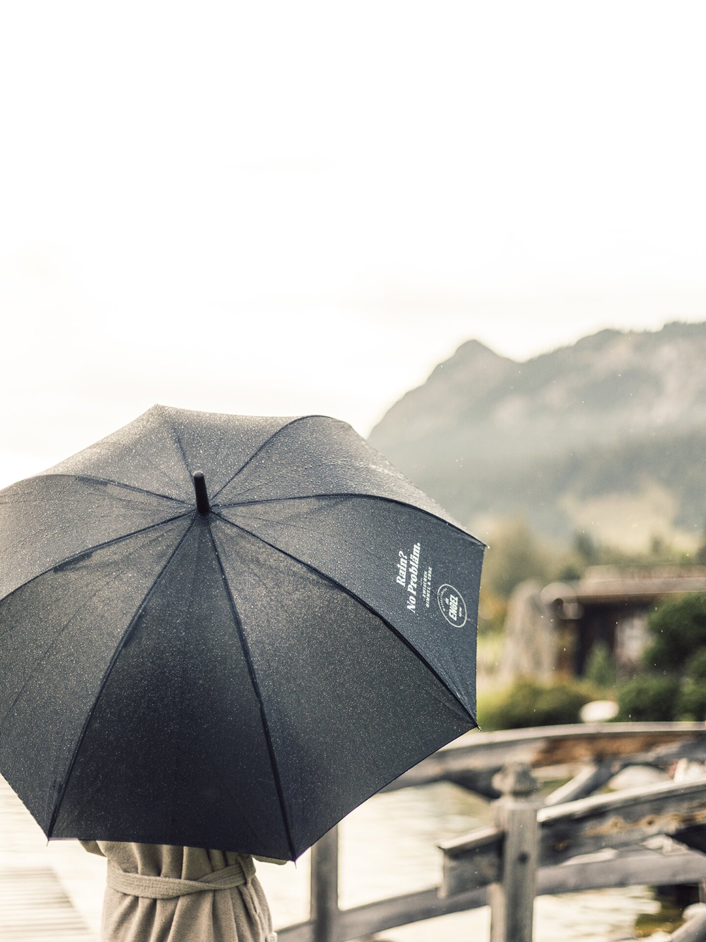 Frau mit Regenschirm am Naturpool des Wellnesshotel Der Engel in Tirol an einem regnerischen Frühlingstag