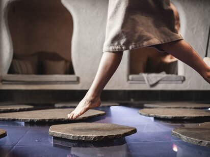 Person springt von Stein zu Stein im Biotop | Wellness-Winterurlaub im Tannheimer Tal