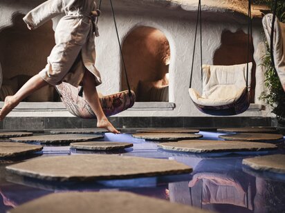 Person in a bathrobe jumping from stone to stone in the biotope | Wellnesshotel Der Engel