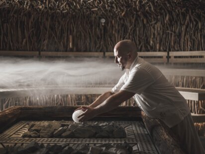 Saunameister Jens legt vorsichtig aromatisierte Eiskugel auf Saunaofen
