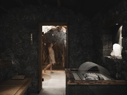 Wellness guest walking in front of the stone house sauna with the sauna door open
