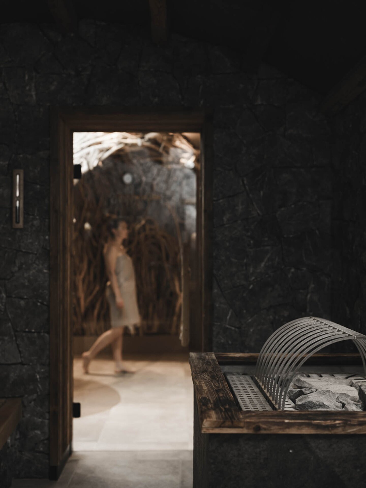 Wellnessgast bewegt sich vor Steinhaus-Sauna bei geöffneter Sauna-Tür