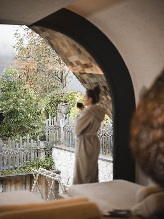 Person im Bademantel mit Teetasse steht vor dem Fenster im Raum der Stille