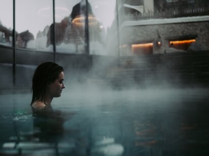 Person bei Sonnenaufgang im Pool - der Dampf des Wassers geht auf