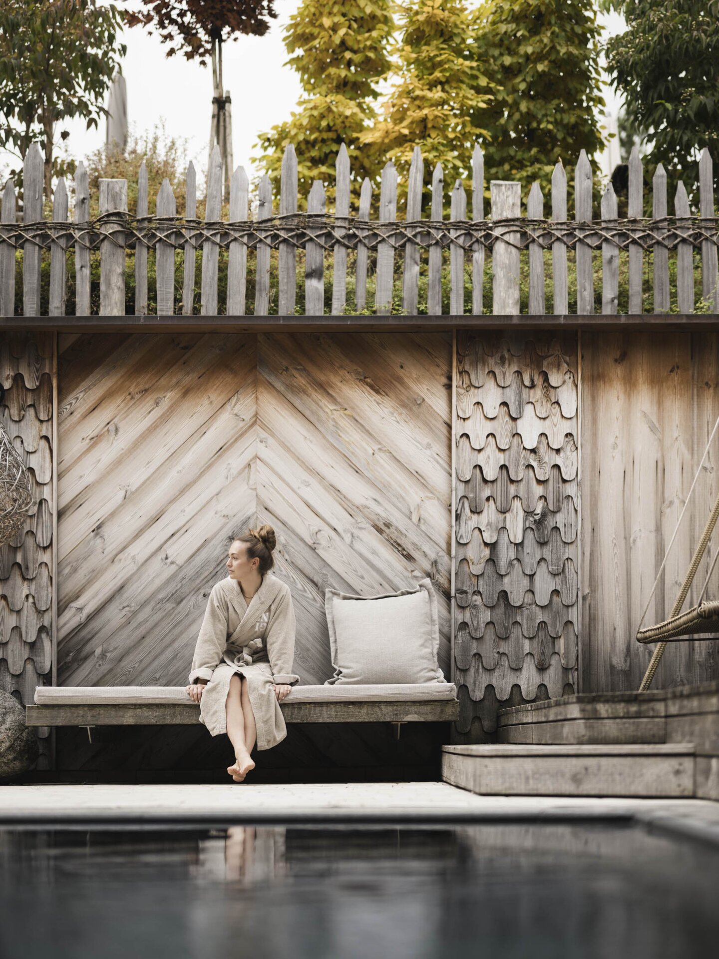 Person im Bademantel sitzt auf Holzbank gegenüber von der Eventsauna