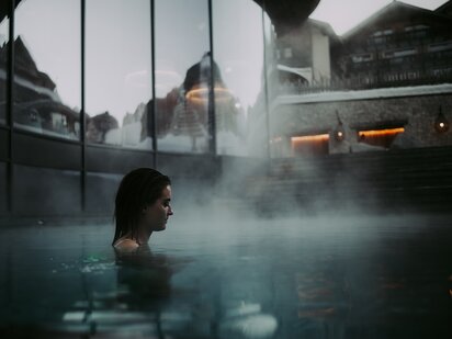 Person im Entspannungspool im Winter mit Glasfassade des Organic Spa | Der Engel in Tirol