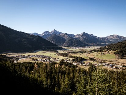 Ausblick vom Berg auf den Ort Grän im Tannheimertal im Frühling mit angezuckerten Bergspitzen | Der Engel in Tirol