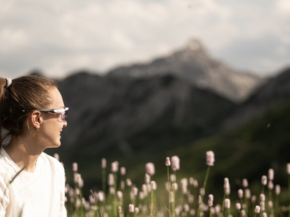 Frau mit Sonnenbrille auf einer blühenden Bergwiese vor den Tiroler Alpen