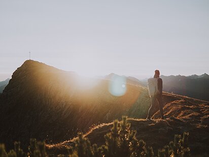 Person beim Wandern in Sonnenuntergangs-Stimmung am Rückenaufbau zu einem Berggipfel im Herbst im Tannheimer Tal 
