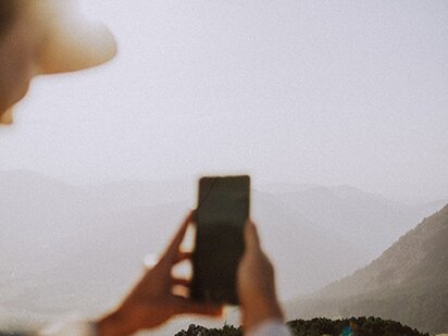 Person fotografiert am Berg mit dem Handy den Sonnenuntergang