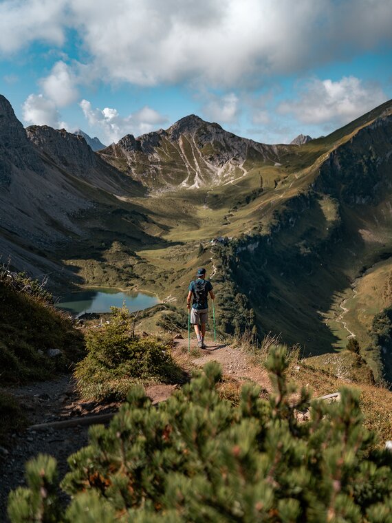 Basti Heckl wandert auf einem Wanderpfad zur Schochenspitze - im Hintergrund die Berglandschaft und ein türkiser See