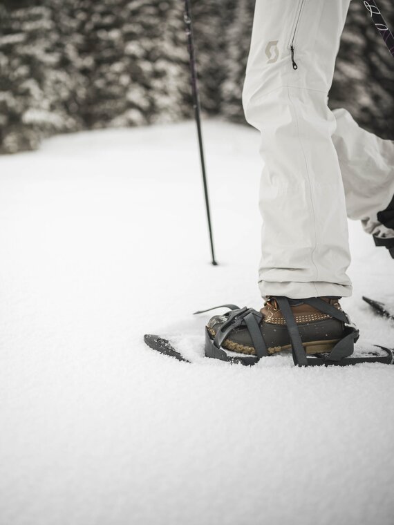 Person beim Schneeschuhwandern in beigem Winteroutfit mitten im Wald
