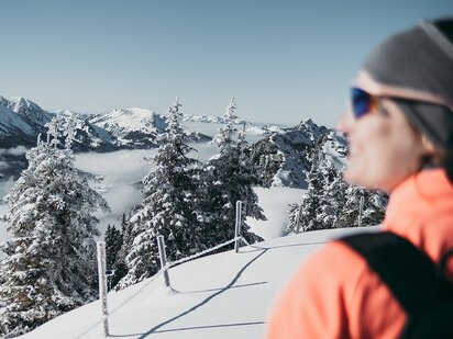 Frau beim Schneeschuhwandern mit Blick auf den Nebel der über dem Tannheimer Tal liegt
