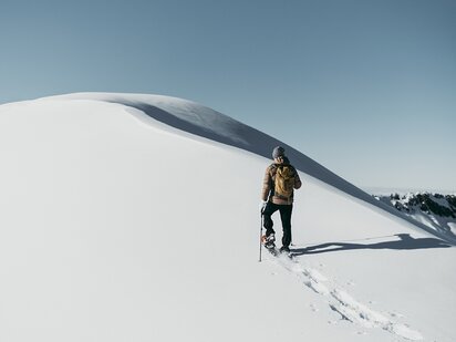Person wandert mit Schneeschuhen auf einem Gipfel im Winter im Tannheimer Tal
