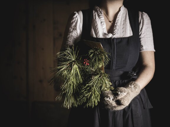 Mitarbeiterin im Dirndl im Wellnesshotel Der Engel hält Kieferzweige in der Hand und hat Handschuhe an - Weihnachtliche Stimmung