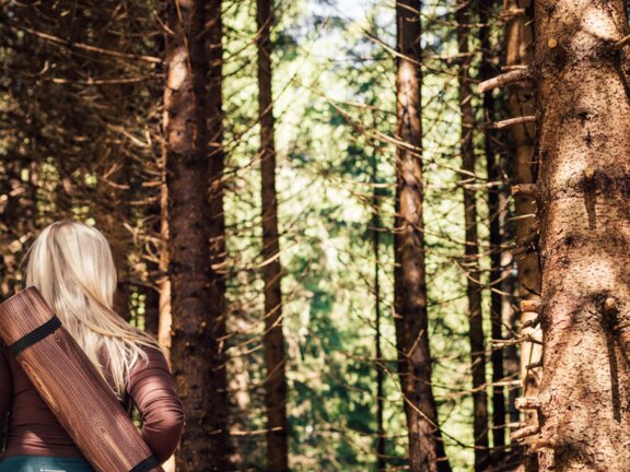 Yoga-Lehrerin mit umhängender Yoga-Matte im Wald