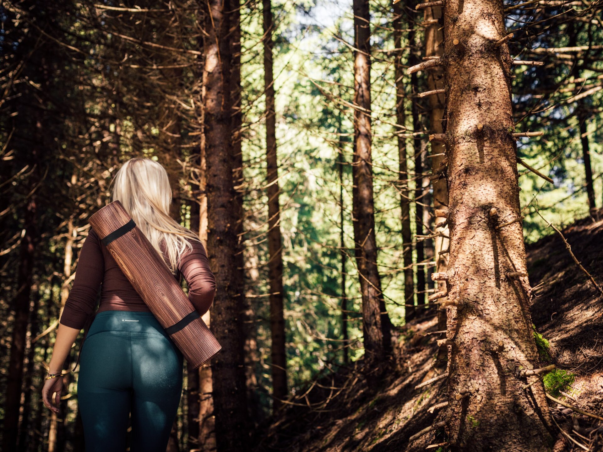 Yoga-Lehrerin mit umhängender Yoga-Matte im Wald