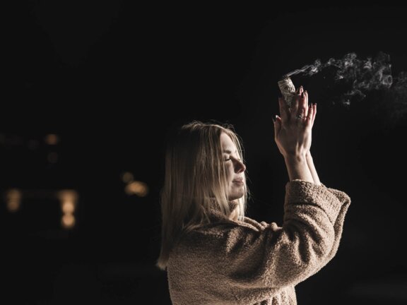 Person im Winter mit Räucherstäbchen in der Hand und gefalteten Händen vor der Brust