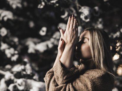 Person mit gefaltenen Händen vor der Brust (Yogapose) im Winter mit kuscheligem braunen Pulli im Außenbereich des Wellnesshotel Der Engel