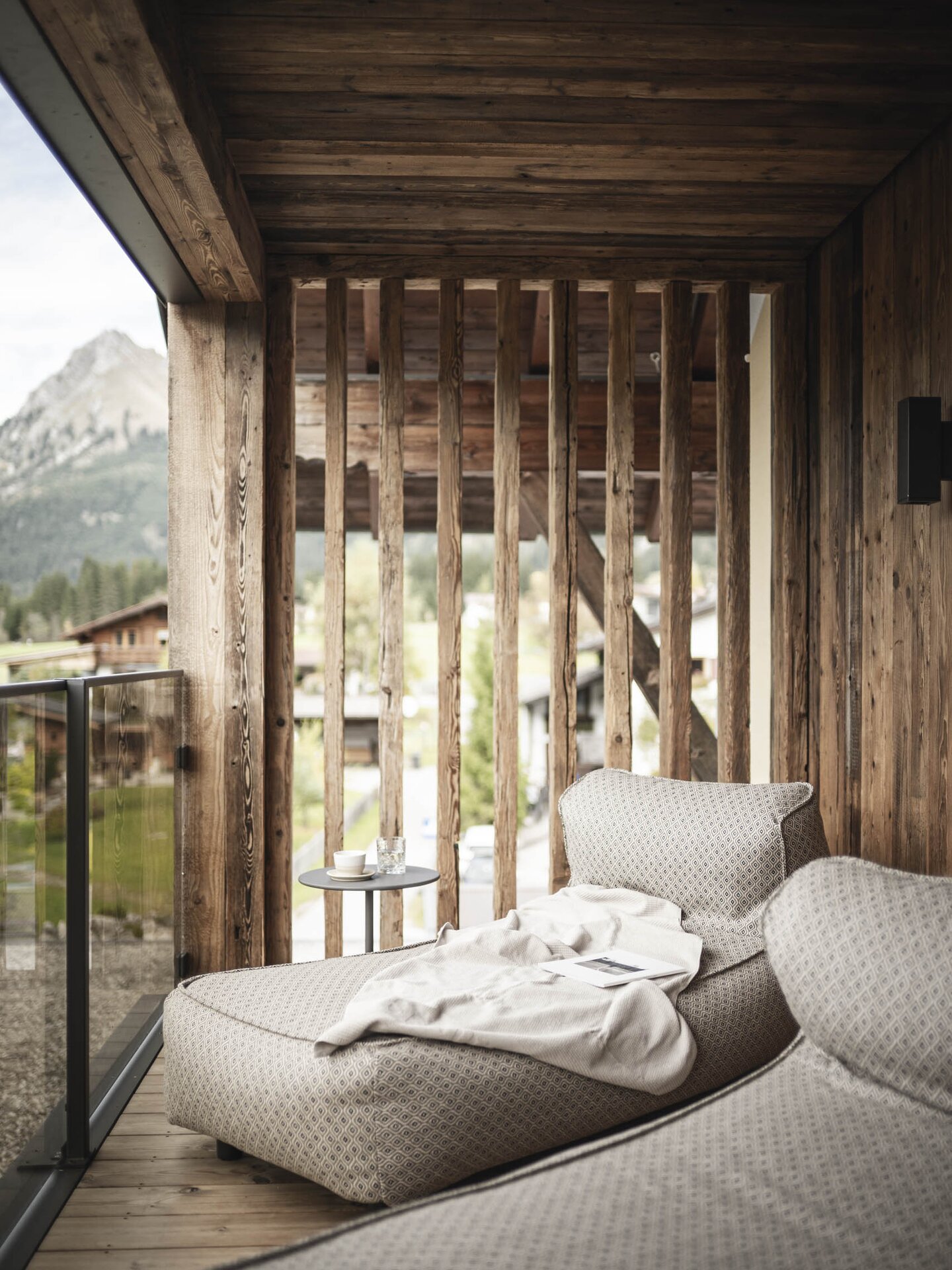 Balkon mit Aussicht auf die Berge, aus Altholz mit dunklem Glas und Daybed | Hoteldesign