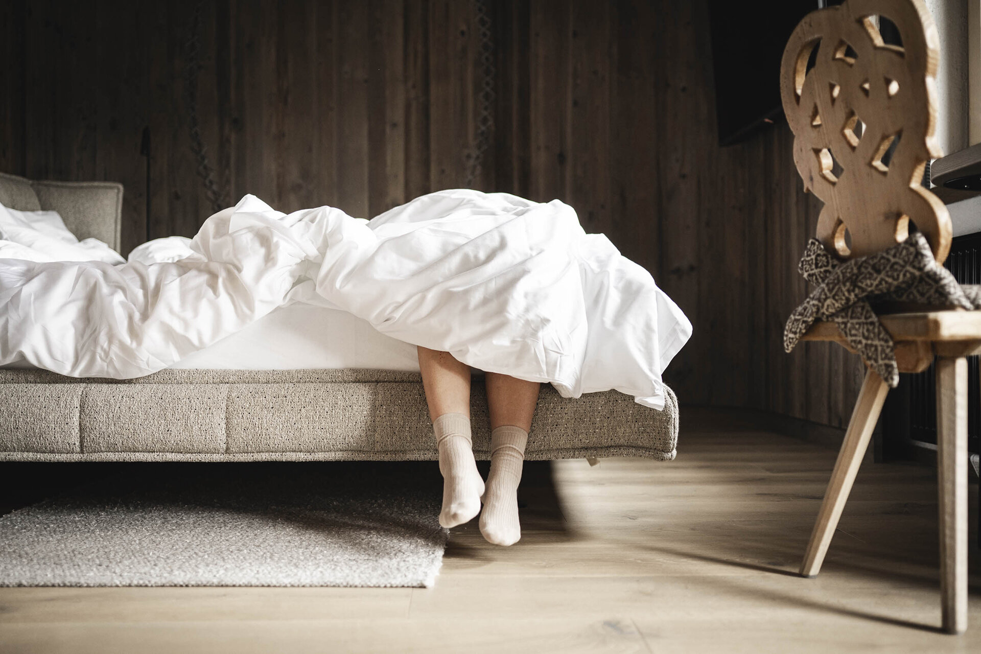 Person liegt im Bett des Orgänic Zimmers, die Beine baumeln aus dem Bett und daneben steht ein traditioneller Holzstuhl