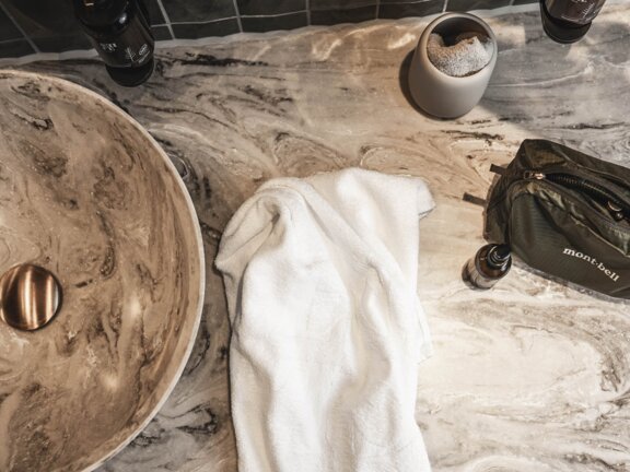 Detailaufnahme vom Orgänic Zimmer Waschtisch mit marmoriertem Stein, grünen Fliesen und grünem Toilettebeutel