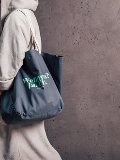 Wellnessgast im Bademantel mit Engel Wellnesstasche vor brauner Wand im Orgänic Spa